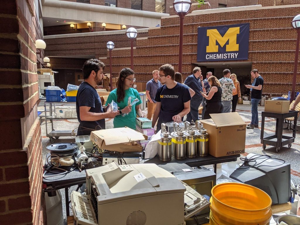 three people converse next to a table full of lab supplies