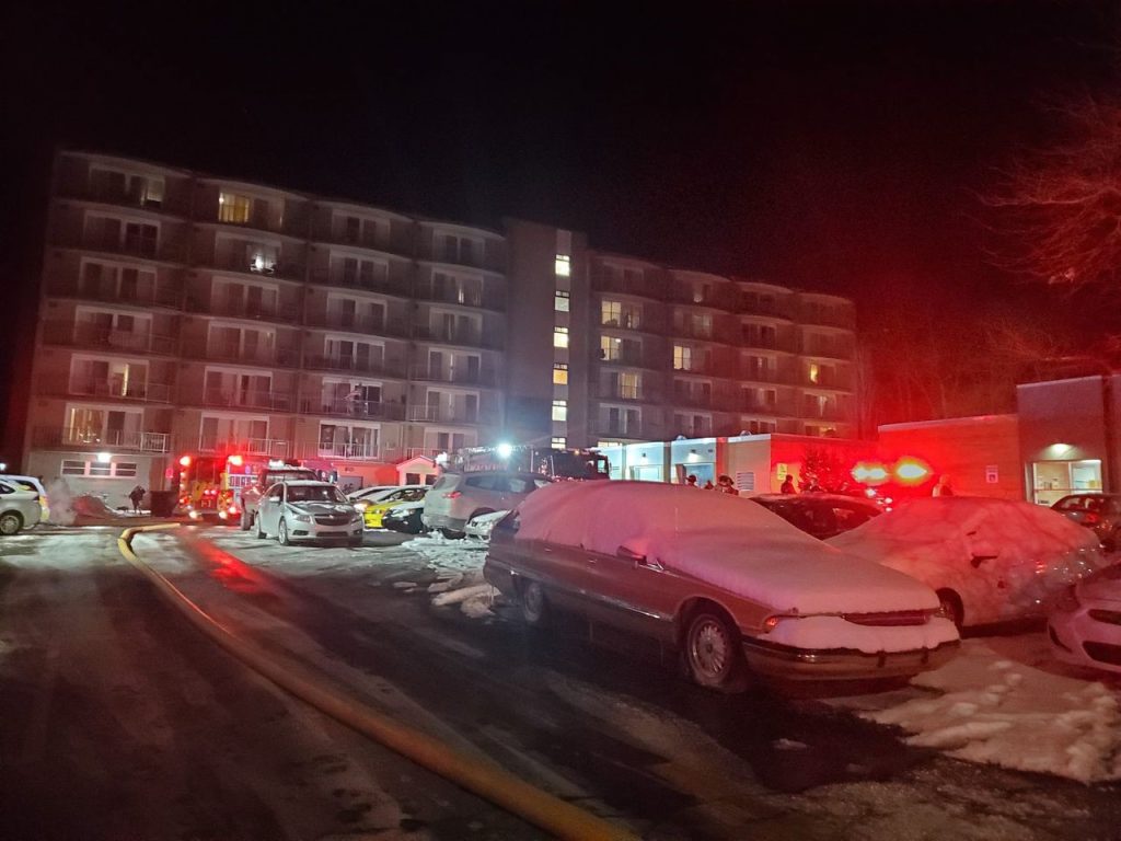 the red lights of fire trucks light up 
snow-covered cars outside an apartment building