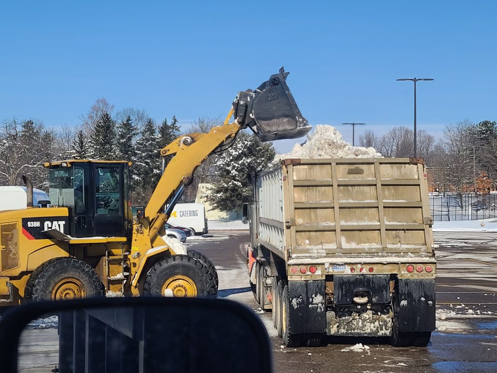 a front-end loader dumps snow into a dump truck